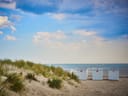 Strand mit Dünen und weissen Strandhütten unter blauem Himmel.