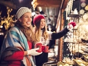 Zwei Frauen lächelnd auf einem Weihnachtsmarkt mit Tassen und Dekorationen.