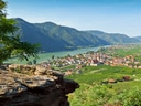 Blick auf ein Tal mit Fluss, Bergen und einer kleinen Stadt mit roten Dächern.