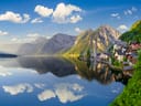 Bergdorf am ruhigen See mit Spiegelung und Bergen im Hintergrund.