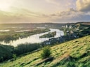 Fluss mit Dorf und Hügeln im Sonnenuntergang.