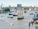 Mehrere Schiffe auf einem Fluss mit Stadt im Hintergrund.