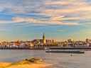 Flusslandschaft mit Stadt im Hintergrund und Frachtschiff auf dem Wasser.