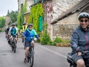 Gruppe von Radfahrern auf einer schmalen Strasse nahe bewachsener Hauswand.