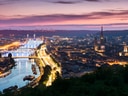 Stadtansicht bei Sonnenuntergang mit Fluss und beleuchteten Gebäuden.