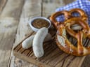 Holzbrett mit Brezeln, Weisswürsten und Schüssel mit Senf.