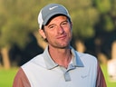 Person mit grauem Hut und Poloshirt steht auf einem Golfplatz.