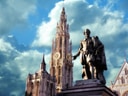 Statue vor Kathedrale mit Uhrturm und bewölktem Himmel.