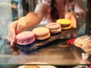 Frau reicht Tablett mit bunten Macarons.