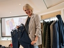 Frau hält Jeans vor einem Kleiderständer in einem Raum.