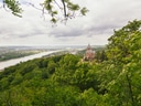 Blick auf ein Schloss inmitten von grünen Bäumen mit einem Fluss in der Ferne.