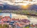 Panoramablick auf Fluss, Dorf mit Kirche und Hügel bei Sonnenuntergang.