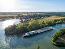 Flusskreuzfahrtschiff fährt auf einem Fluss durch eine ländliche Landschaft.
