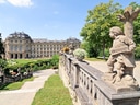 Rokokogebäude mit Garten und Statue im Vordergrund.