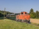 Roter Zug fährt durch grüne Landschaft.