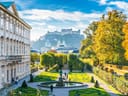 Ein Schlossgarten mit gepflegten Hecken, einem Brunnen und Blick auf eine Festung im Hintergrund.