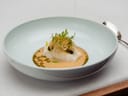 Gourmetgericht mit Fisch in heller Schale auf Tisch mit Löffel.