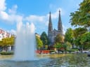 Springbrunnen mit Kirche im Hintergrund an einem sonnigen Tag.