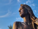 Bronzestatue einer Frau vor blauem Himmel.