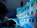 Beleuchtetes historisches Gebäude mit Wandmalereien bei Nacht, Brücke über Wasser.