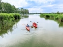 Zwei Kayaks auf einem Fluss in grüner Umgebung.