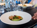 Fein angerichteter Teller mit Vorspeise bei einem eleganten Abendessen, Hände greifen nach Besteck.