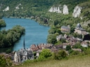 Malerisches Dorf an Fluss mit grünen Hügeln und weissen Felsen.