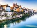 Flussufer in Basel mit historischen Gebäuden und Kirche.