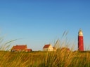 Roter Leuchtturm und Häuser hinter Graslandschaft.