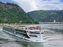 Kreuzfahrtschiff auf einem Fluss zwischen bewaldeten Hügeln.