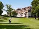 Person spielt Golf vor einem grossen Gebäude auf einem grünen Feld.