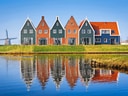 Traditionelle Häuser und Windmühle am Flussufer mit Spiegelung.