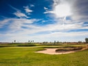 Sonniger Golfplatz mit Sandbunker und blauem Himmel.