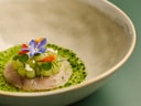Gourmetgericht auf grünem Teller mit Blumen und Kräutern.