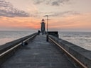 Leuchtturm an einem langen Pier bei Sonnenuntergang mit ruhigem Meer.