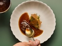 Hand mit Löffel über Teller mit Sauce und Gemüsegericht.