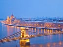 Flusslandschaft bei Dämmerung mit beleuchteter Stadt und Brücke.