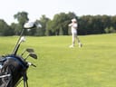 Golfschläger in einer Tasche mit Person im Hintergrund auf einem Golfplatz.