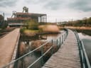 Holzweg führt durch Sumpflandschaft zu alten Industriegebäuden.