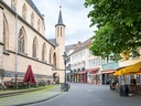 Stadtstrasse mit alten Gebäuden, Sitzgelegenheiten im Freien und Sonnenschirmen.