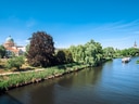 Flusslandschaft mit Boot und Gebäude im Hintergrund unter blauem Himmel.