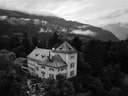 Historisches Gebäude in waldreicher Berglandschaft mit Wolken im Hintergrund.