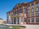 Barockes Gebäude mit Brunnen im Vordergrund an einem sonnigen Tag.
