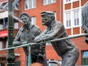 Bronzefiguren zweier Männer, einer spuckt Wasser.