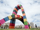 Bunte Container in bogenförmiger Skulptur vor Gebäude.