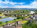 Panoramablick auf Flusslandschaft mit Brücke, Häusern und bewaldeten Hügeln.