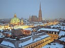 Schneebedecktes Stadtbild mit beleuchteter Kuppel und Turm am Abend.
