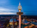 Abendansicht eines beleuchteten Vergnügungsparks mit Turm und Glaskuppel.