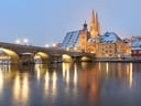 Steinbrücke über einen Fluss mit beleuchteter Altstadt im Hintergrund.