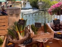 Marktstand mit Gemüse vor einem Fluss und einem grossen Gebäude im Hintergrund.